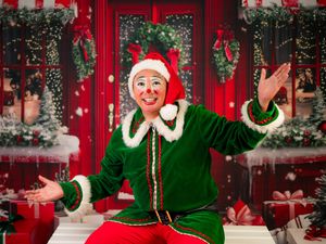 Cheerful clown dressed as an elf in a vibrant Christmas setting.